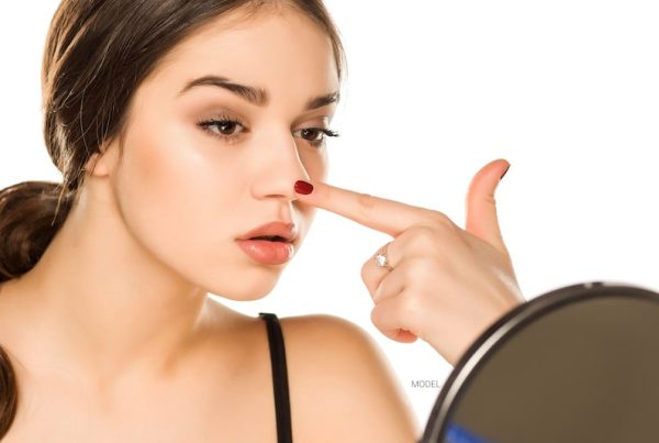 Beautiful woman touching her nose while she looks at her reflection in the mirror